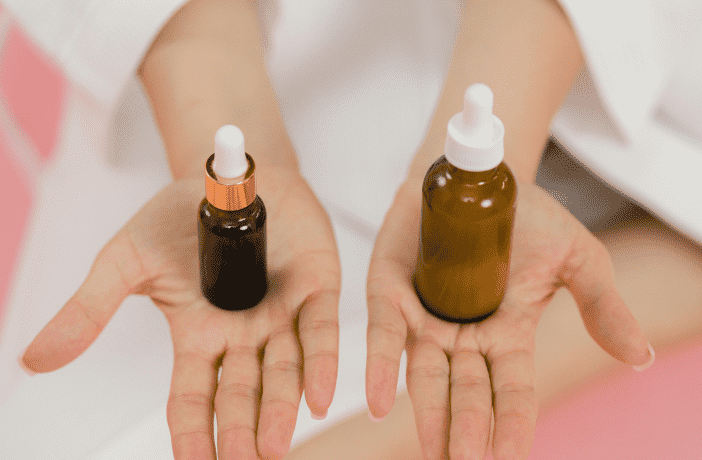 Two hands holding amber glass dropper bottles of different sizes with white and metallic caps.