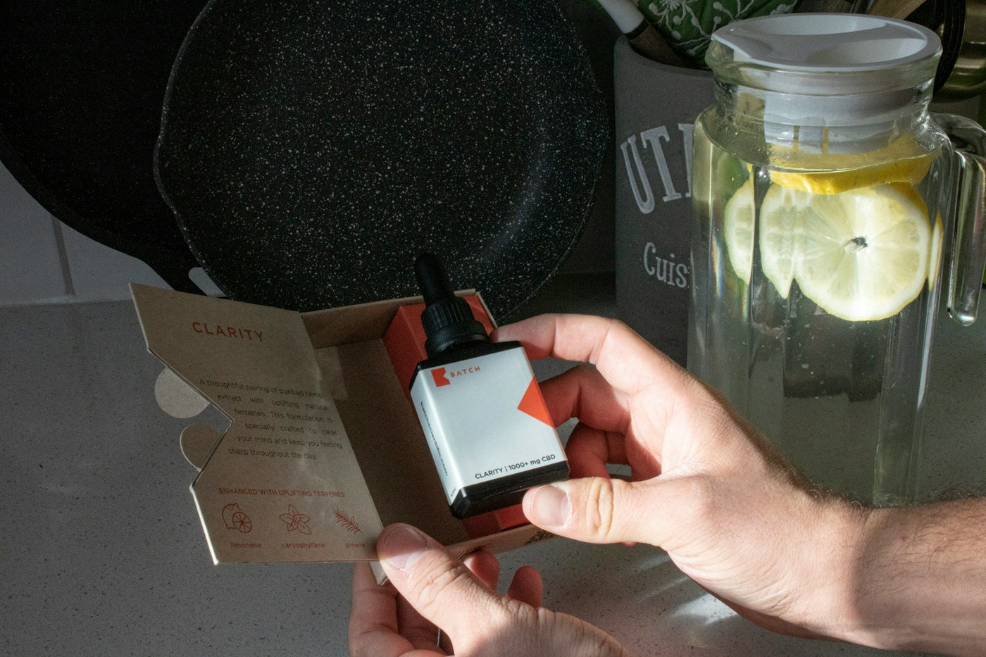 Hands holding a dropper bottle of CBD oil with its open, informative cardboard packaging.