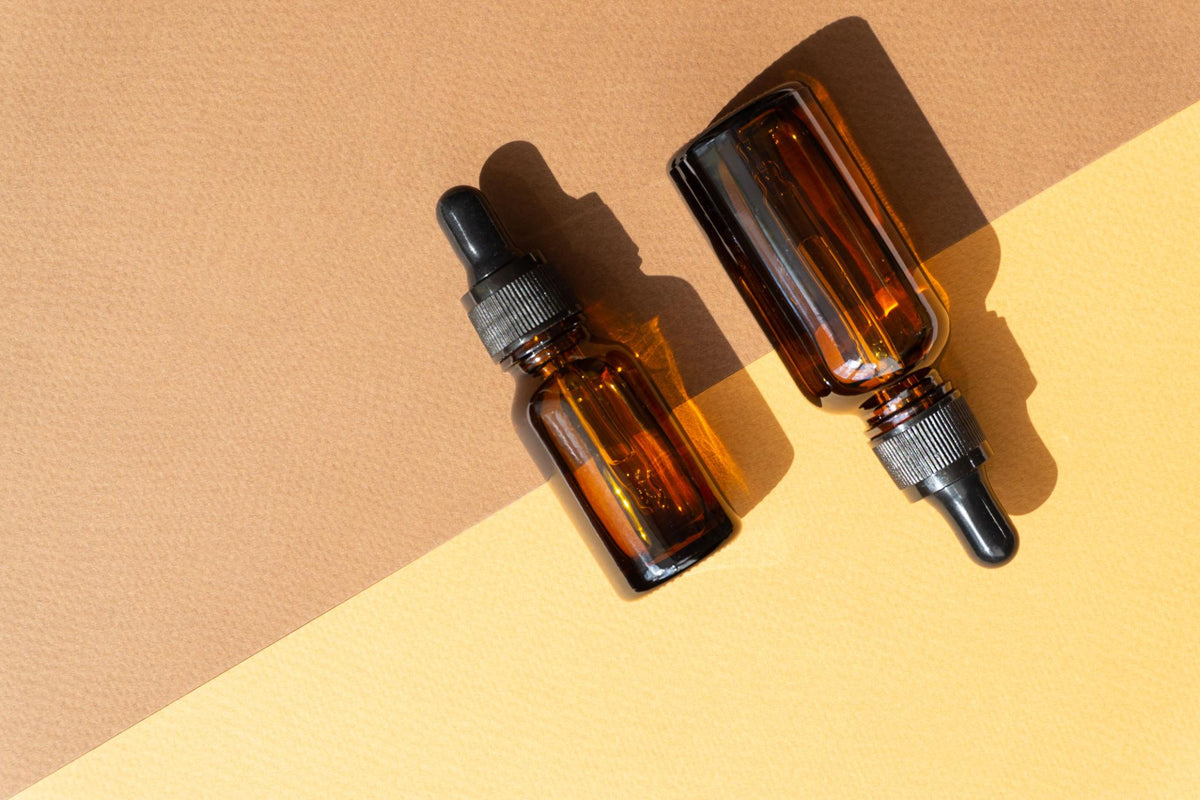Two amber glass dropper bottles with black caps resting on a split-tone beige and yellow background.