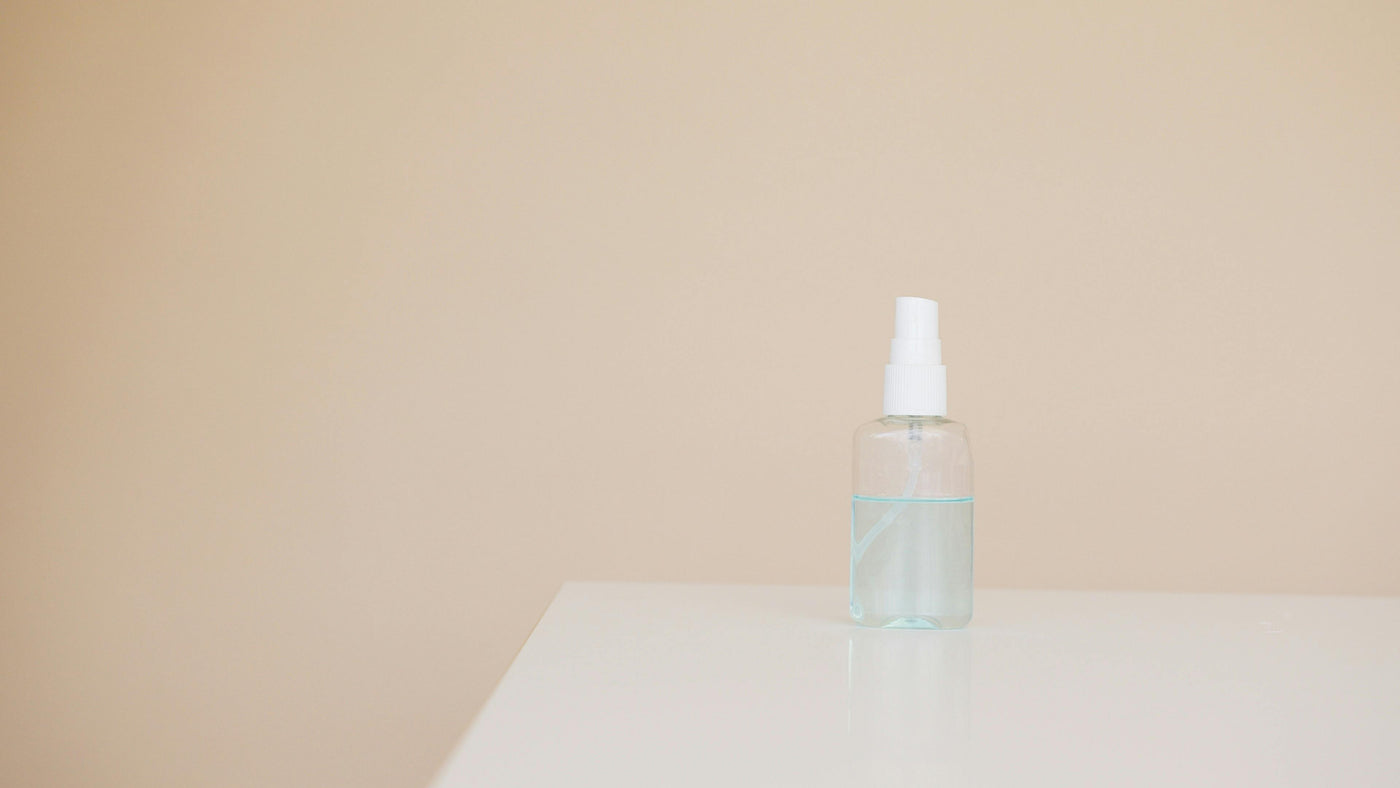 Clear glass spray bottle filled with liquid sitting on a white surface against a neutral beige background.