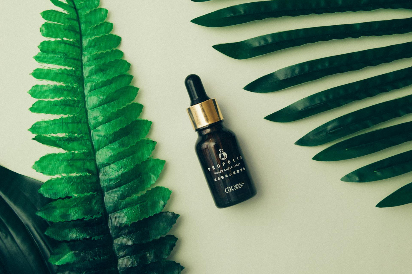 Minimalist amber glass dropper bottle with gold cap placed between green tropical leaves on a light background.
