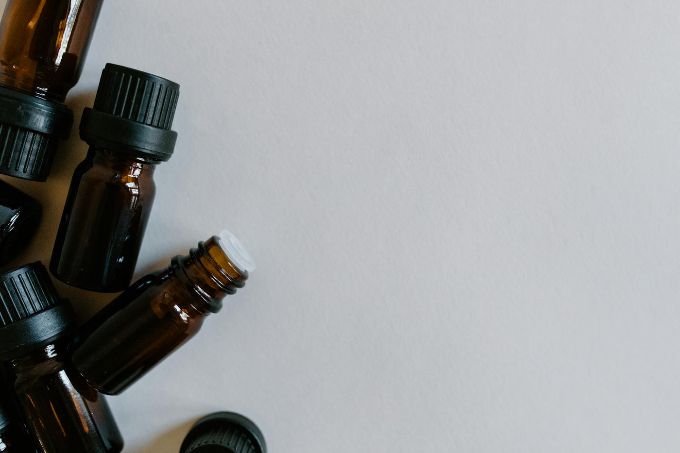 Small amber glass dropper bottles with black caps arranged on a neutral grey background.