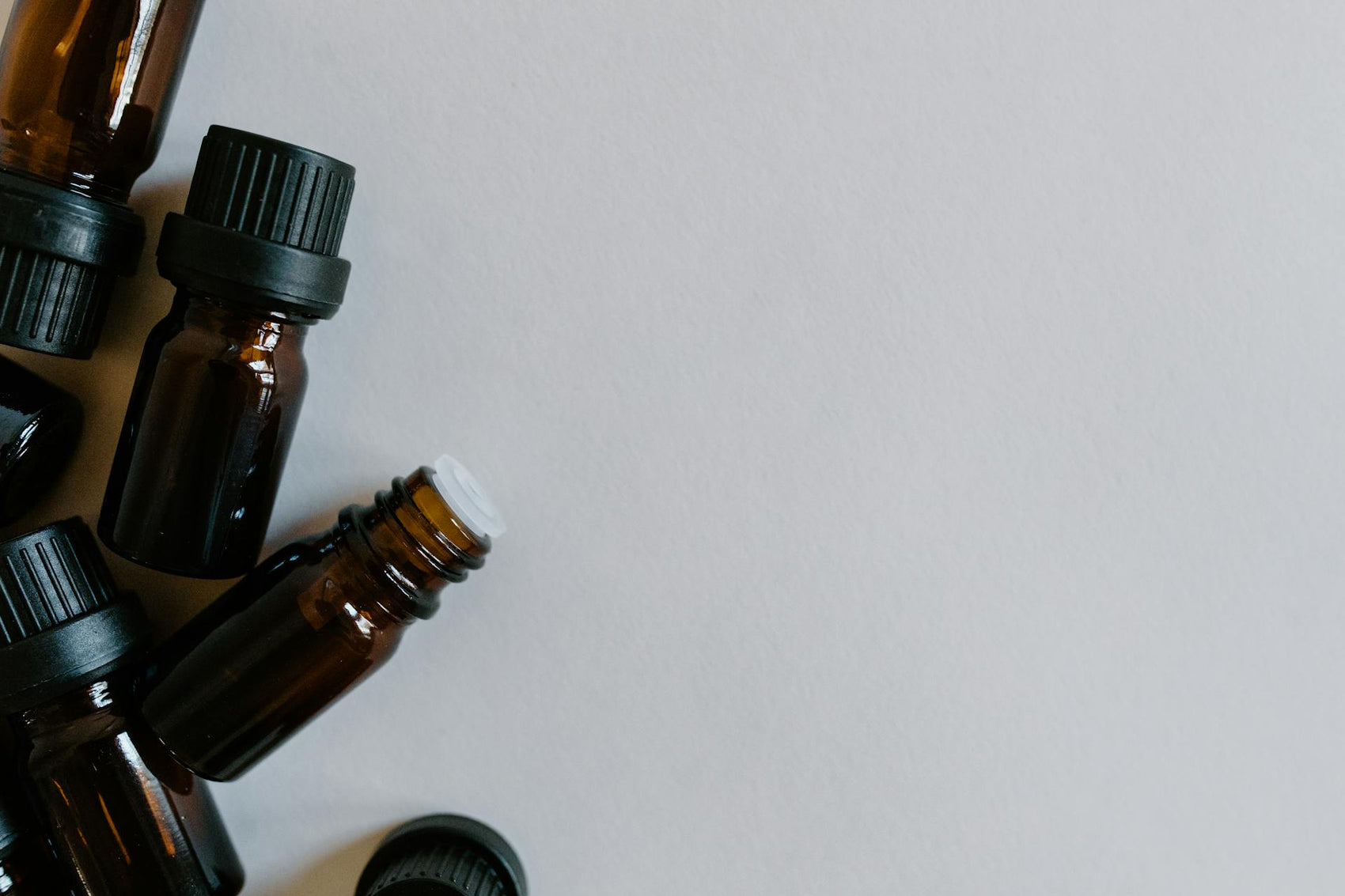 Small amber glass dropper bottles with black caps arranged on a neutral grey background.