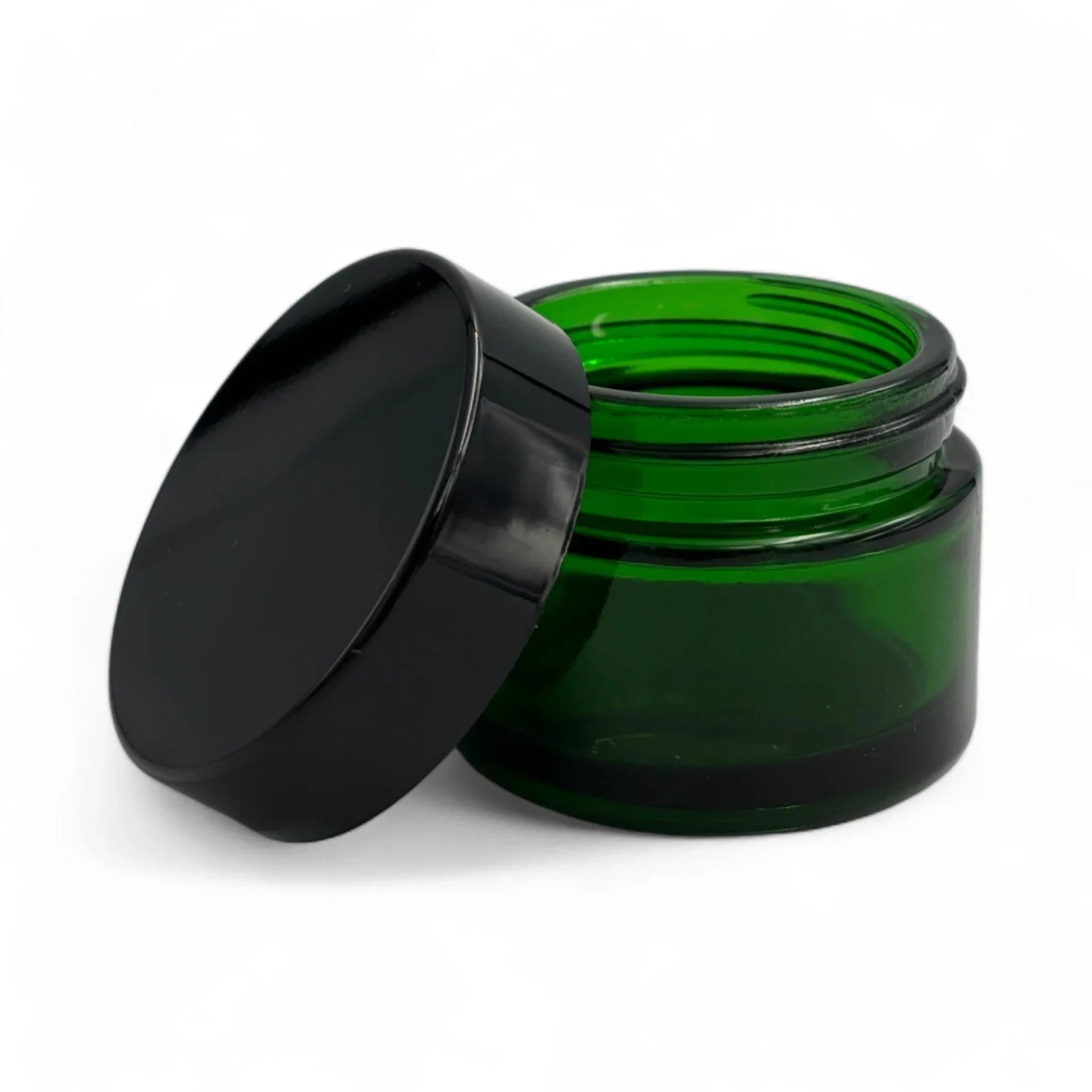 Small emerald green glass cosmetic jar with a sleek black lid isolated on a white background.