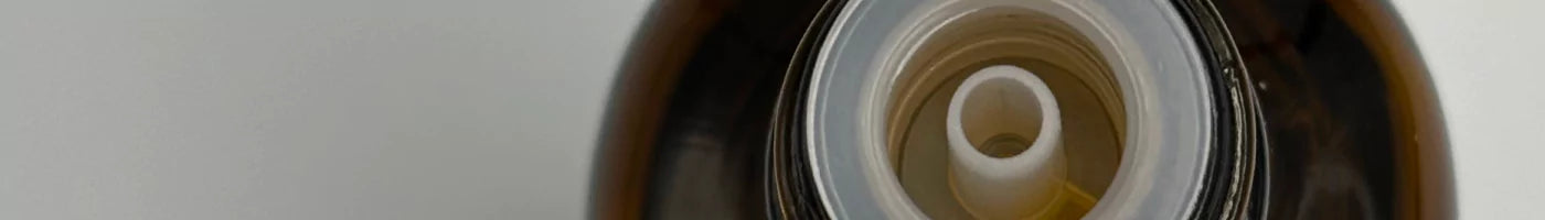 Top-down view of a white plastic dripper insert fitted into the neck of an amber glass essential oil bottle.